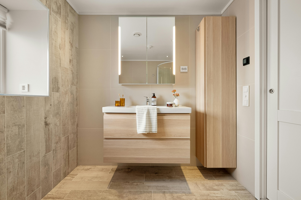 Modern bathroom with wooden vanity, mirror, and cabinets.