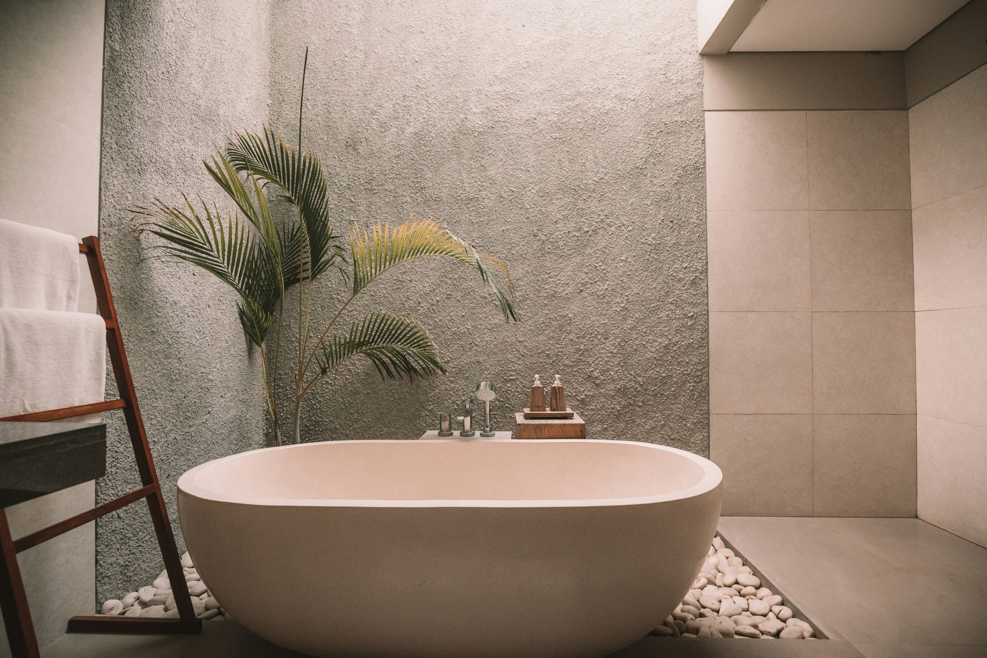 Modern bathroom with a freestanding bathtub, plant, and towels.