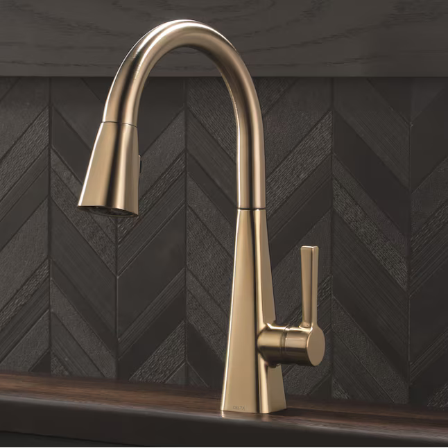 Gold kitchen faucet on a black tiled wall