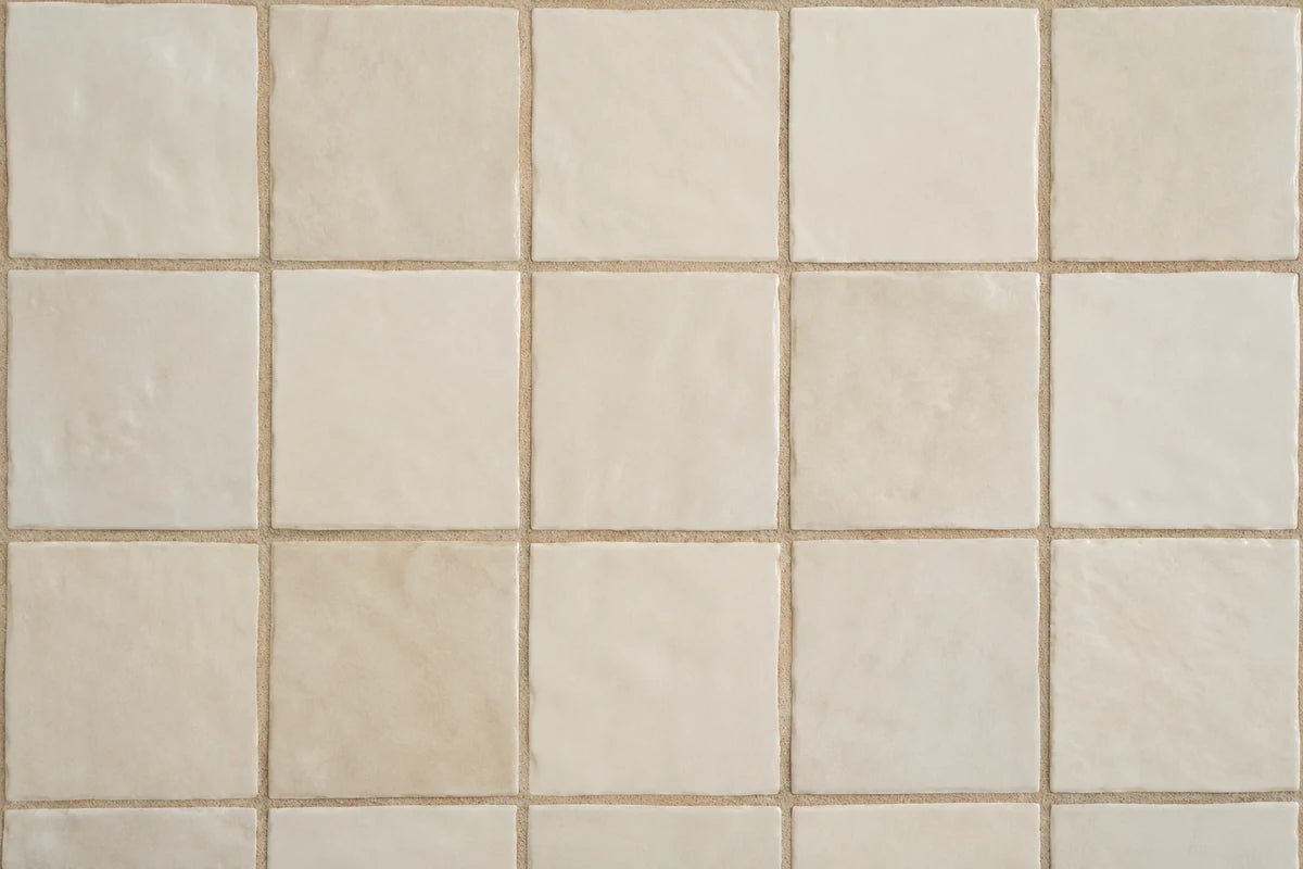Detailed view of warm cream square tile with distinctly beige grout joints, slight handmade surface variation, clean even joints occupy enough frame to read their sand color, neutral soft daylight, no objects