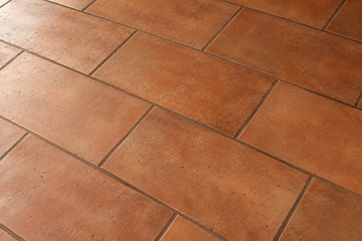 Detailed photograph of terracotta rectangular tile with rich warm brown grout, neat visibly brown joints and matte fired-clay texture, diagonal viewing angle with straight tile geometry, no props