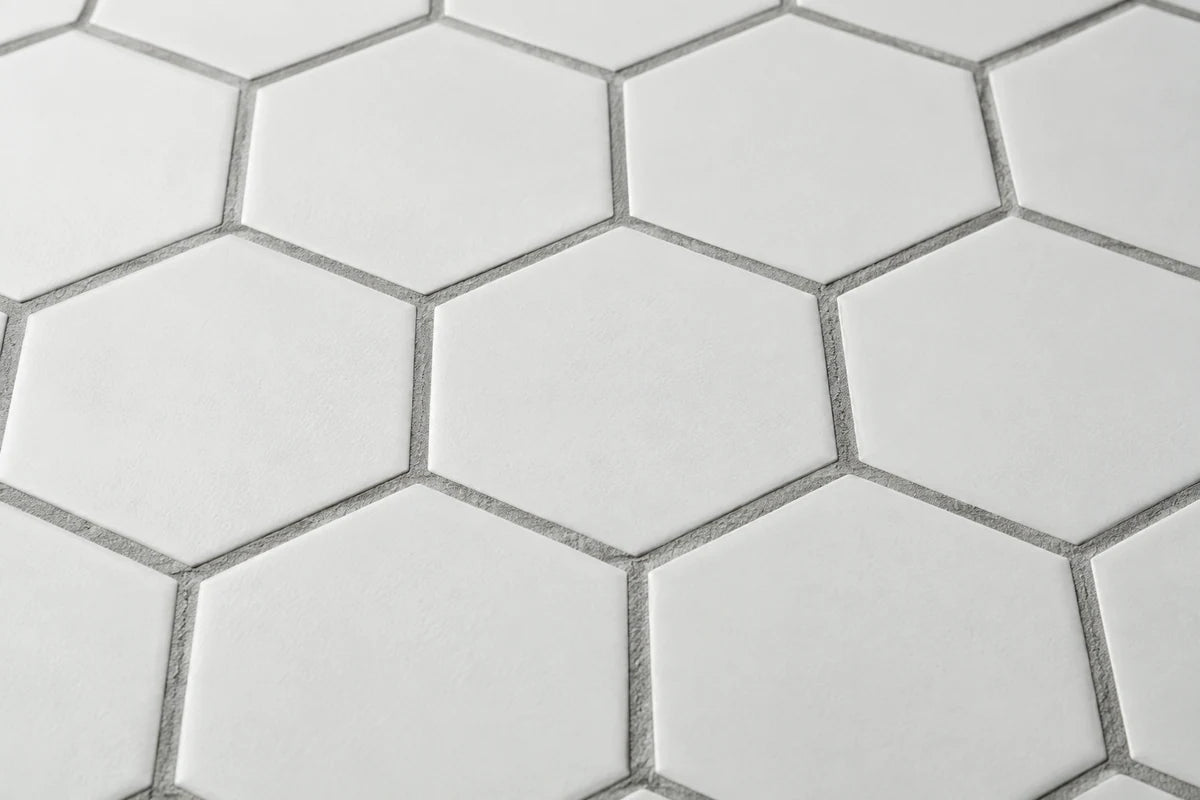 Very close angled photograph of matte white hexagonal tile with medium-gray grout joints, clean consistent grout visibly framing each tile