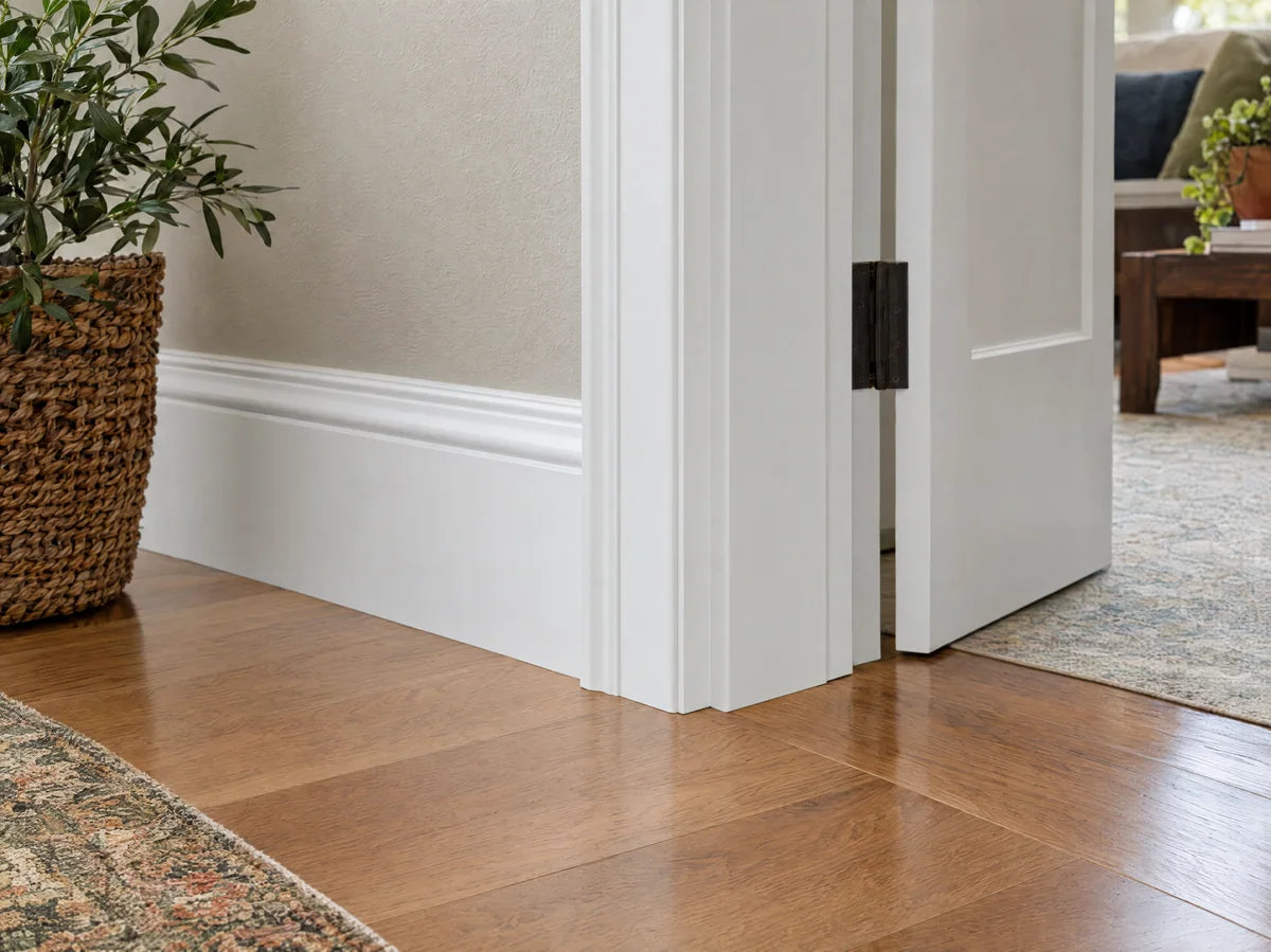 Close view of crisp white painted baseboard and door casing meeting oak floor, perfectly mitered corner, bright architectural detail.