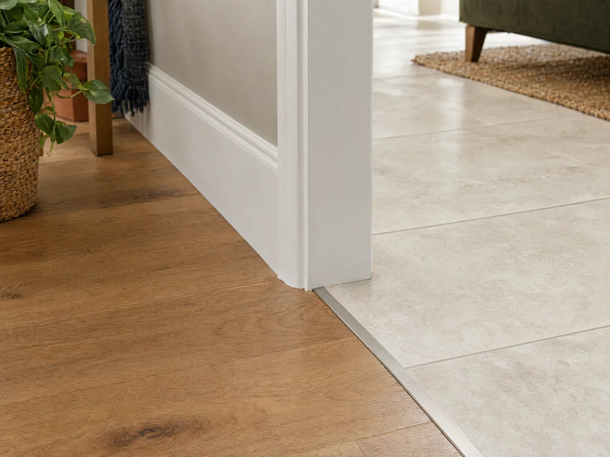 Clean transition between oak floor and ivory tile with a slim metal threshold profile, tight join and white baseboard, macro architectural detail.