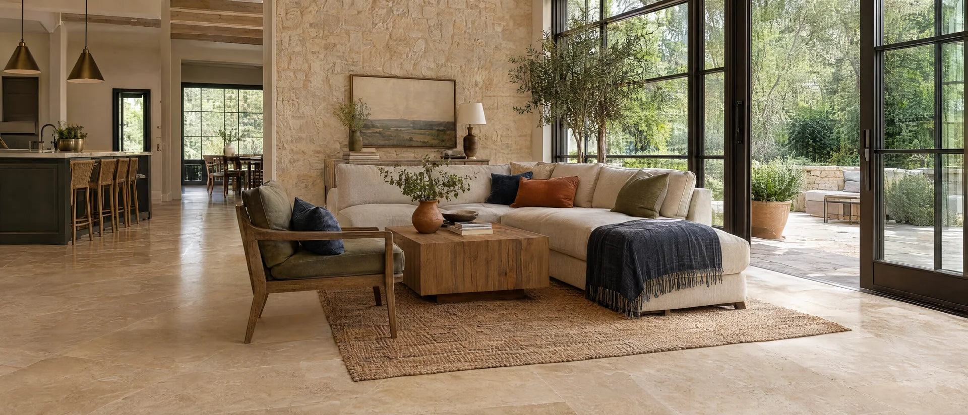 Refined American indoor-outdoor living space with warm honed travertine floor, limestone-textured accent wall and large glass doors toward a green courtyard