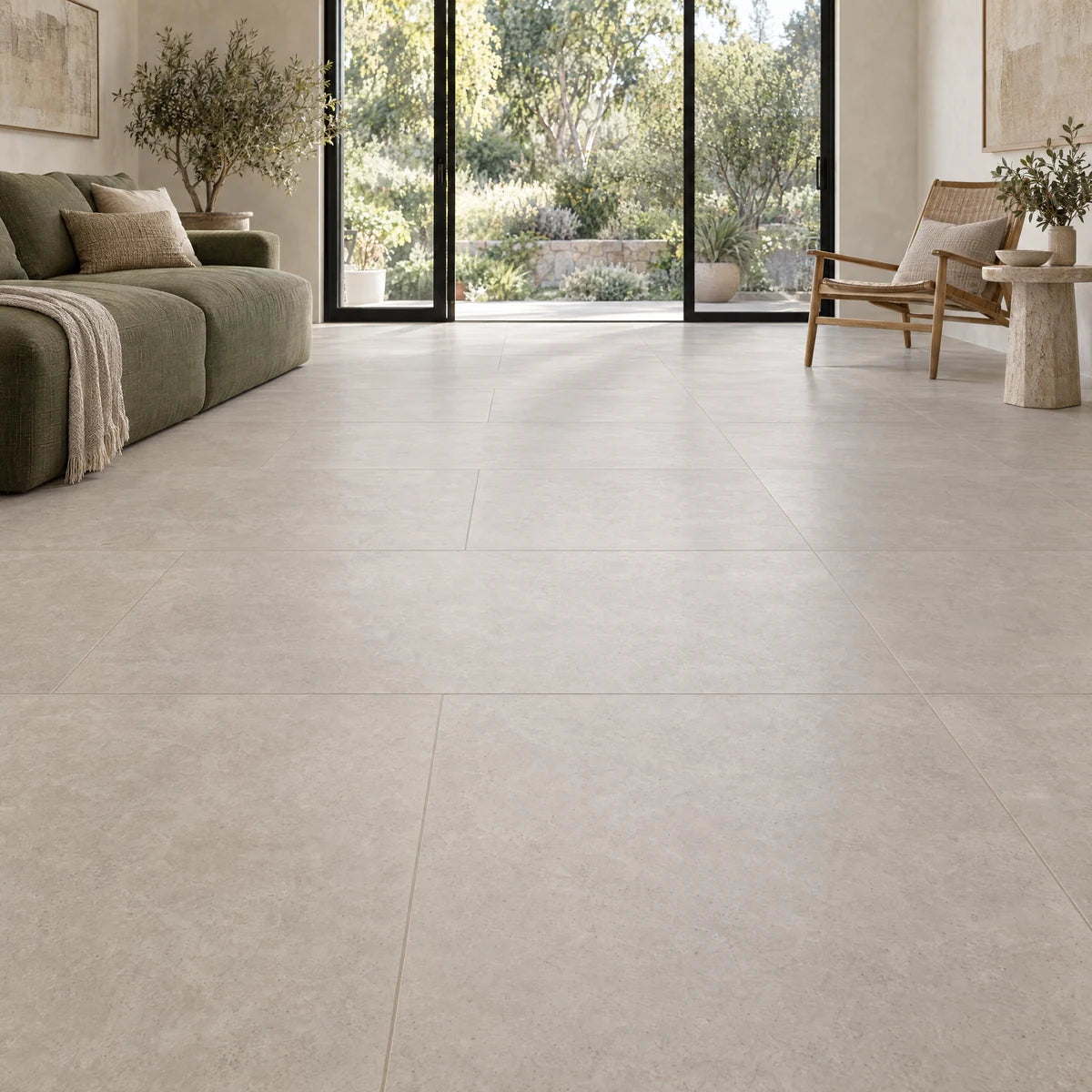 Large-format matte porcelain floor tiles in a living room with an olive sofa and garden doors