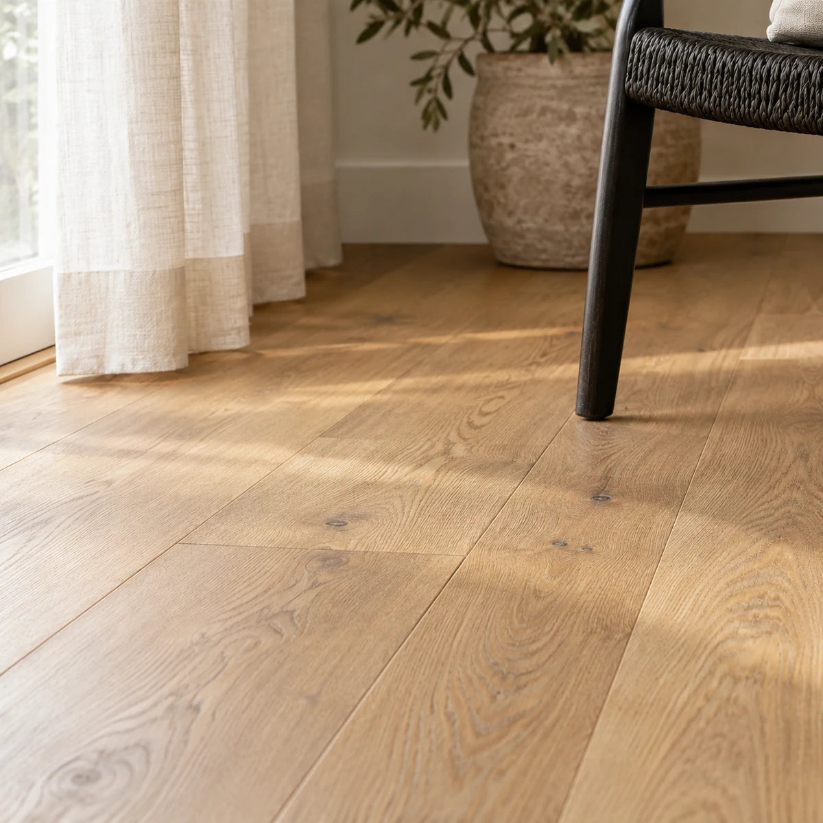 Natural oak grain beside a linen curtain and black woven chair.