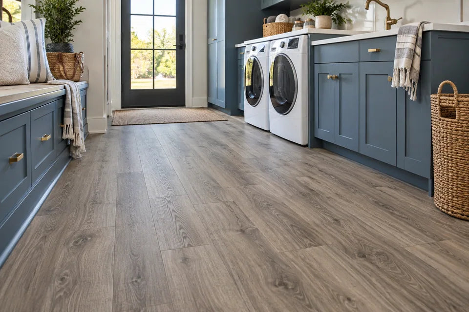 Warm gray wood-look vinyl plank flooring in a bright laundry mudroom with blue cabinetry
